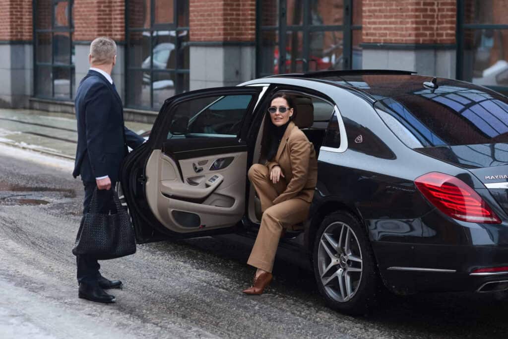 Woman arriving at Logan Airport in a luxury chauffeur-driven car, ready for travel.