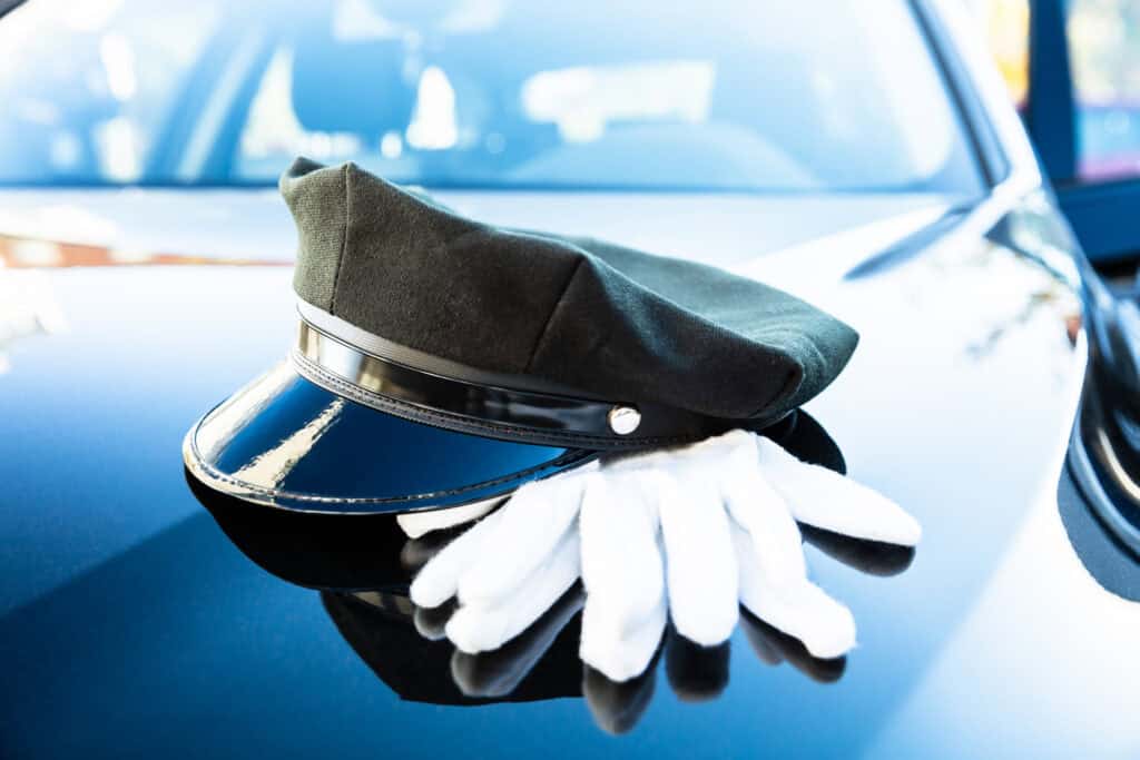 Chauffeur hat and gloves on a luxury car hood for premium chauffeur service.