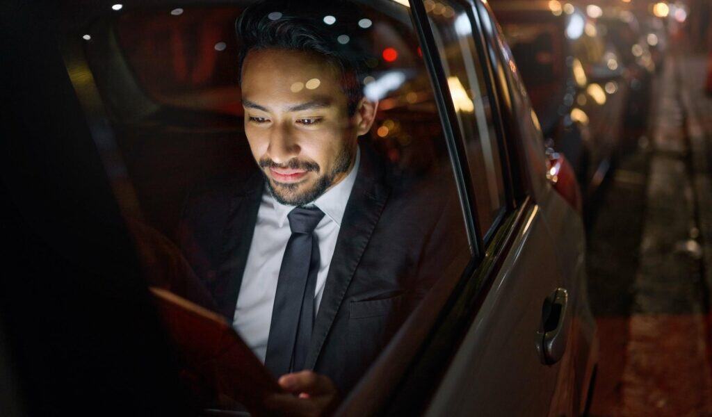 Man in formal suit using a smartphone inside a luxury car at night.