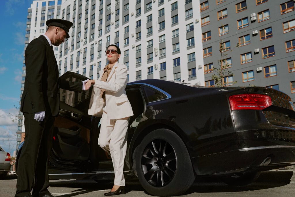 Professional Mak Louren chauffeur assisting a woman with her luggage near a luxury car for a premium airport car service.