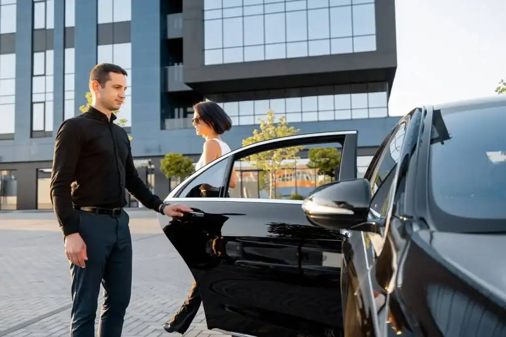 Luxury chauffeur service with professional driver assisting a passenger at a modern office building.