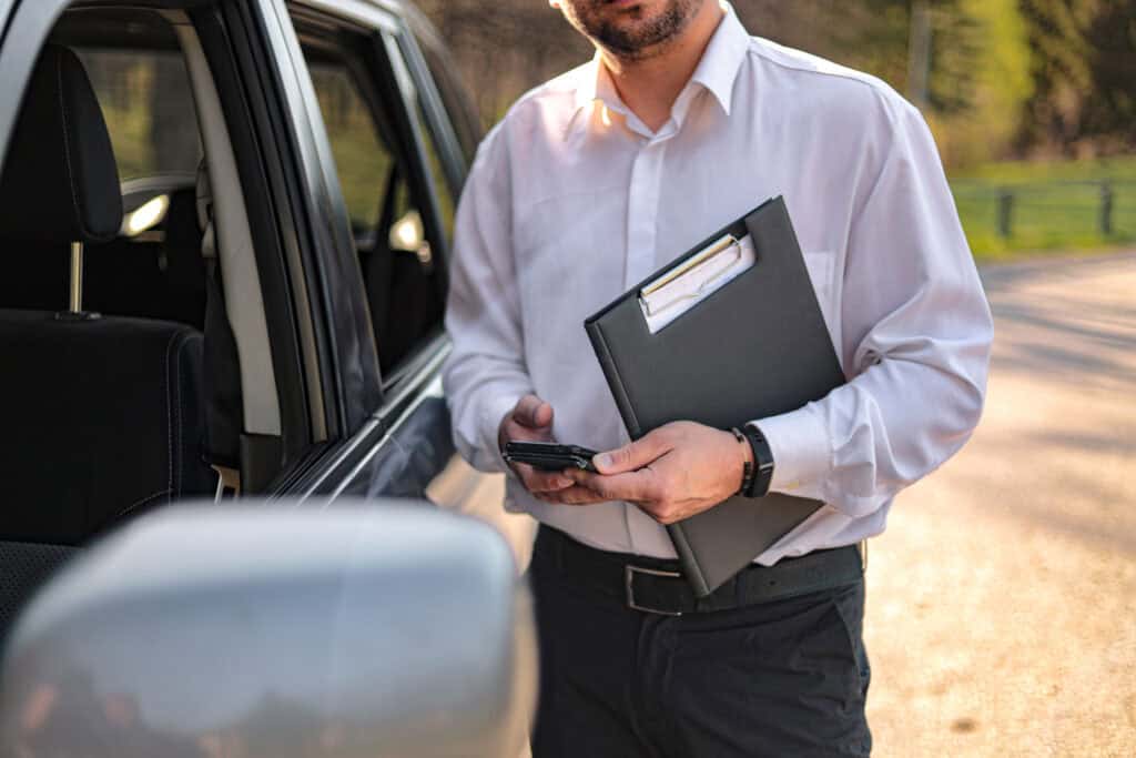 Luxury chauffeur service professional with a clipboard outside a vehicle.