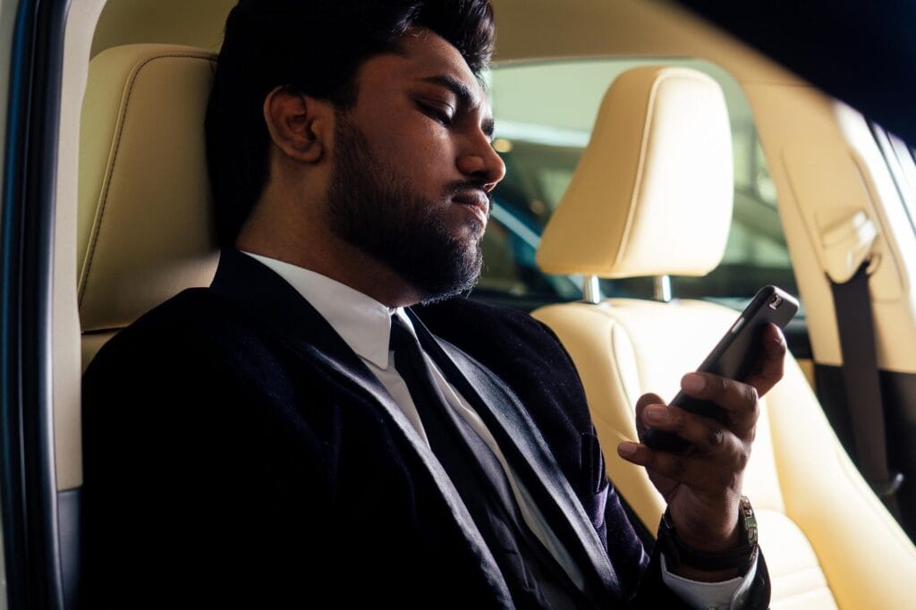 Man using smartphone in luxury car, professional chauffeur service Mak Louren.
