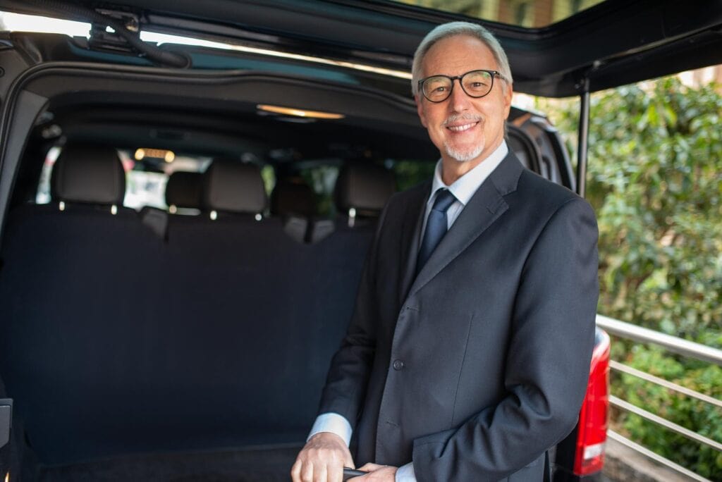 Professional chauffeur in formal suit standing beside a luxury vehicle.