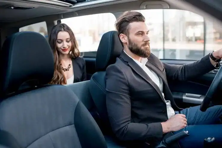 Professional chauffeur driving with a passenger in the back seat of a luxury vehicle.