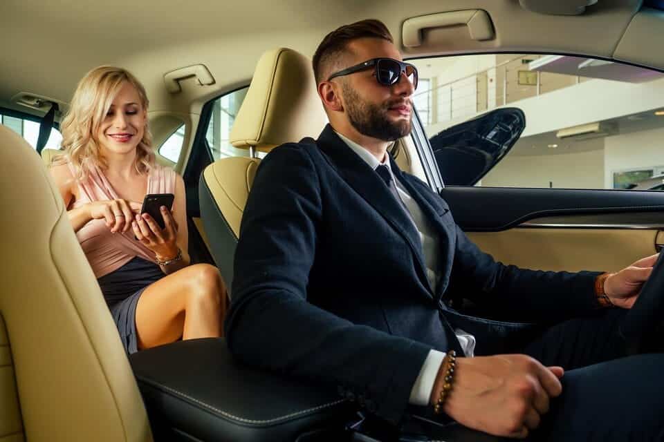 Professional chauffeur driving luxury car with smiling woman passenger using smartphone.